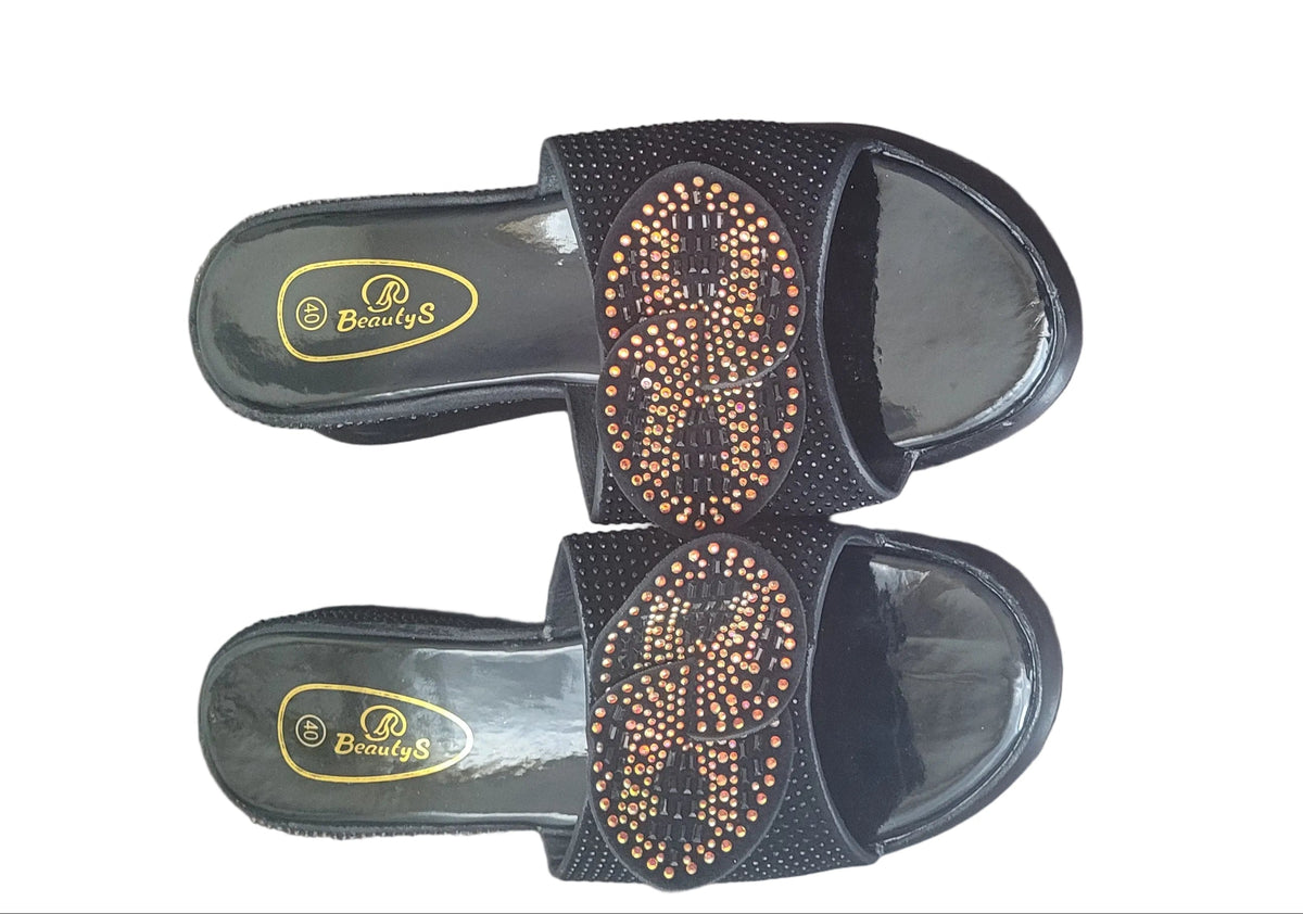 A pair of black slide sandals with a textured upper strap embellished with gold rhinestones, displayed on a dark wood floor. The brand name 'Piyera' is visible on the footbed.
