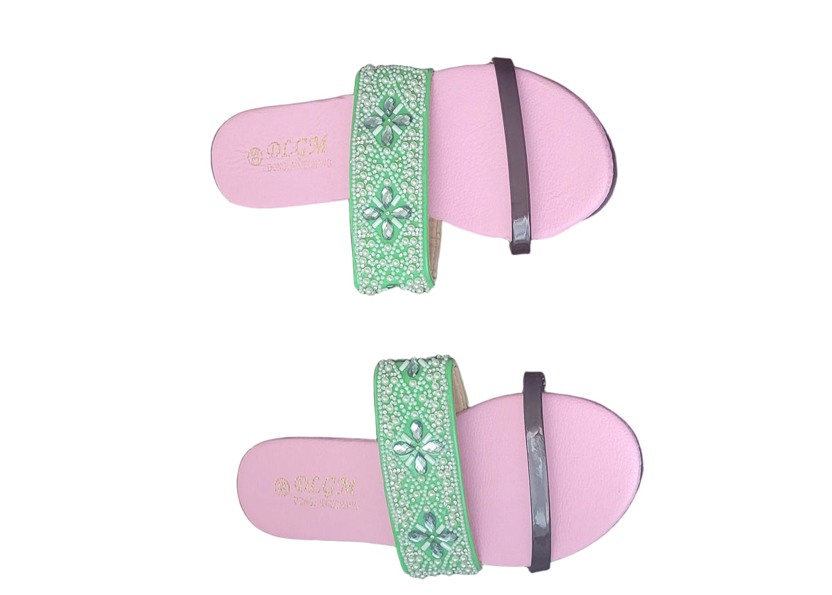 A pair of pink slide sandals with green embellished straps, placed on a dark wood floor. The brand name 'SOUKOU' is visible on the insole of each sandal.