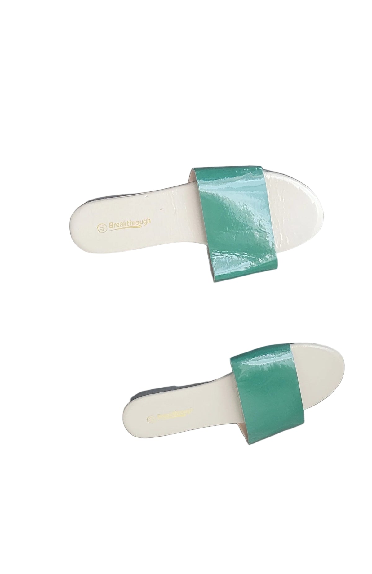 A pair of white slide sandals with shiny green straps, placed on a dark wood floor.