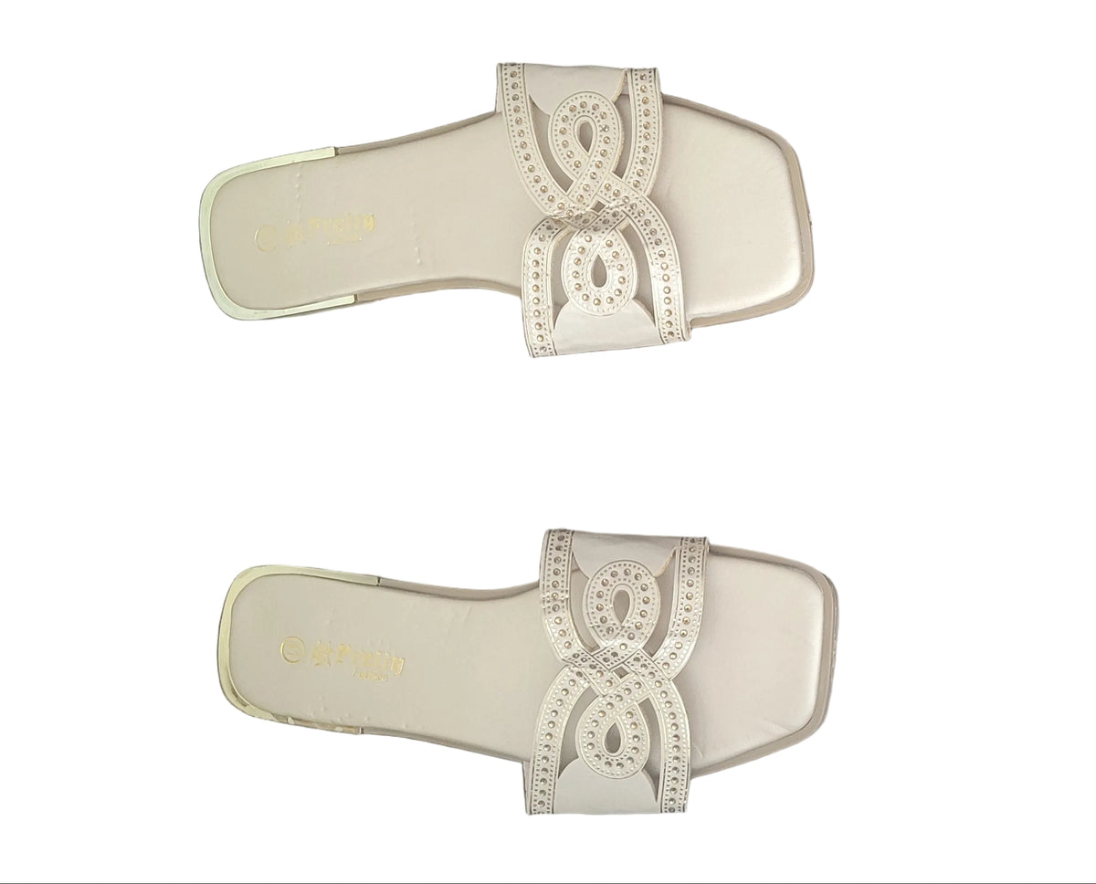 A pair of off-white slide sandals with decorative bow details on the straps, shown from above on a dark wood floor.