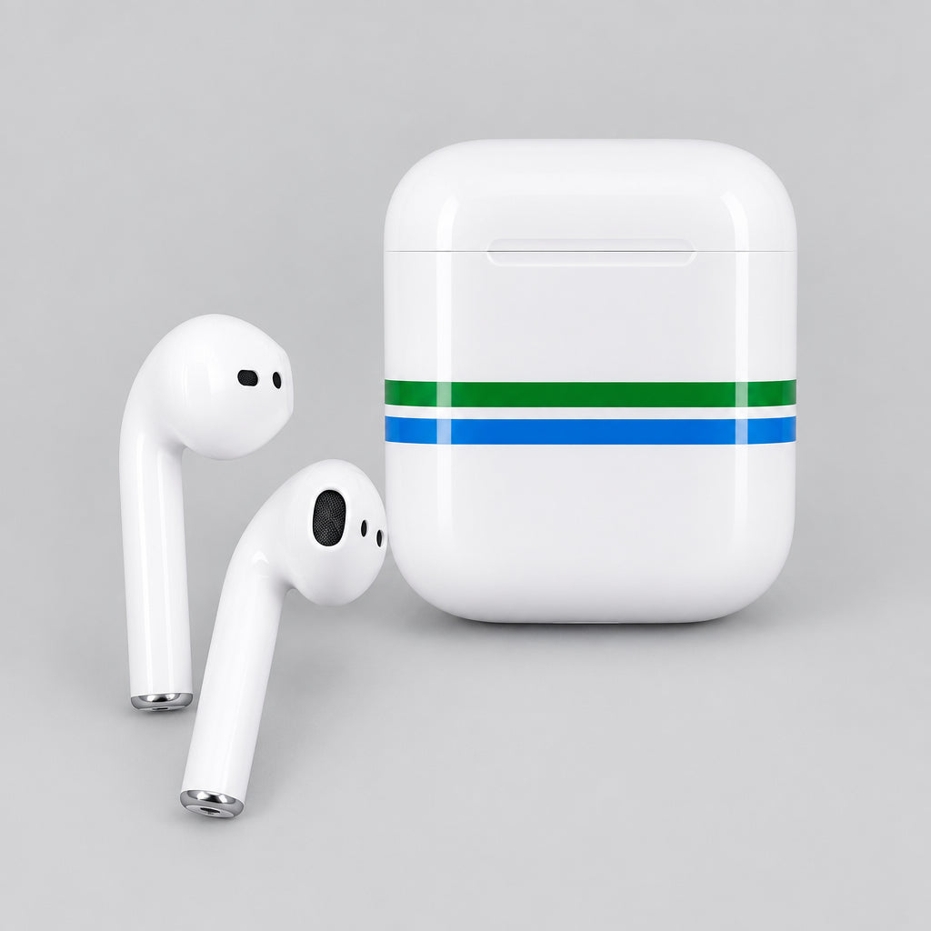 A hand holding a pair of white wireless earbuds and their charging case, with the case decorated by green and blue tape. The background shows a cluttered desk with various items and a Realme phone box.