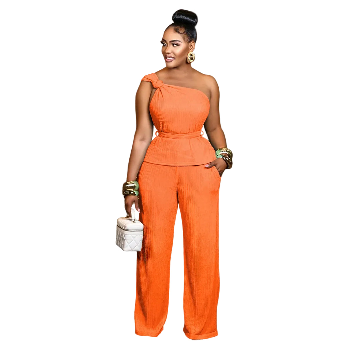 A woman models a bright orange one-shoulder jumpsuit in a modern indoor setting. The jumpsuit features an asymmetrical shoulder design, a fitted waist, and wide-leg pants.