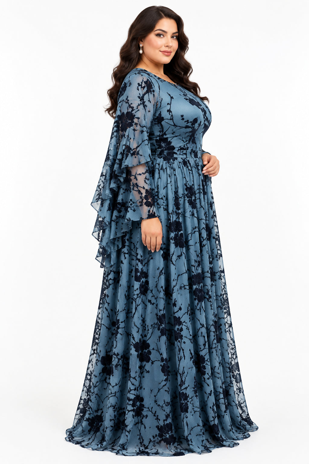 A long-sleeve blue maxi dress with a black floral branch print, displayed on a mannequin in an indoor boutique setting. The dress features a fitted bodice, a flared waist, and a flowing skirt.
