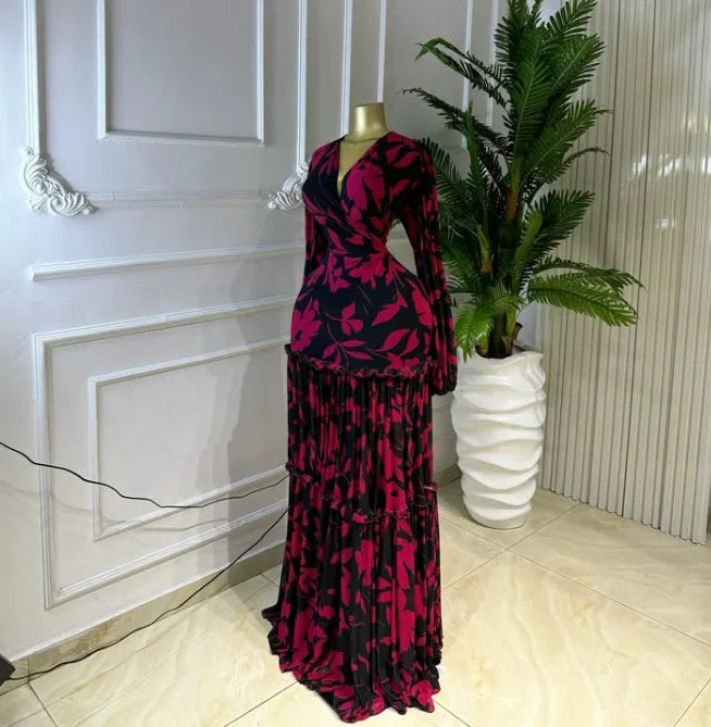 A long-sleeve maxi dress with a deep V-neck and tiered ruffle skirt, featuring a bold magenta and black floral pattern, displayed on a mannequin in an indoor setting.