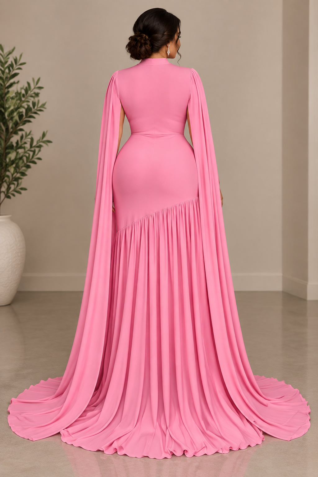 A pink floor-length gown displayed on a mannequin in an indoor setting with beige curtains and a wooden floor. The dress has long sheer sleeves, a fitted bodice, a high neckline, and a flared pleated skirt with a train.