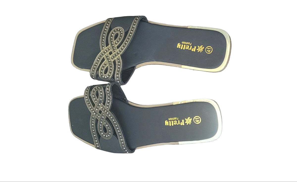 A pair of women's slide sandals with dark gray straps featuring a decorative gold and silver knot pattern, resting on a dark wood floor. The insoles are black with gold branding.
