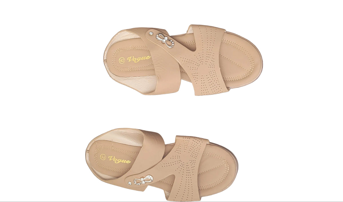 A pair of beige strappy sandals with silver buckle details, displayed on a dark wood floor. The brand name 'Vagabond' is visible in gold lettering on the insoles.