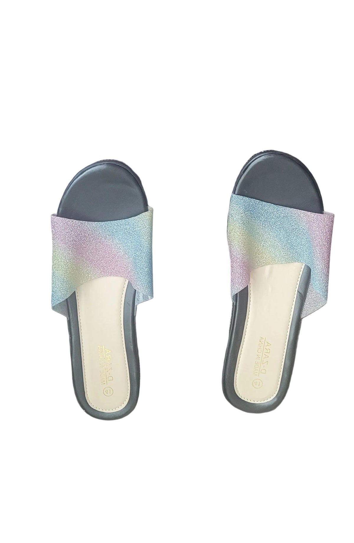 A pair of women's slide sandals with black wedge heels and iridescent pastel rainbow straps, shown on a dark wood floor.