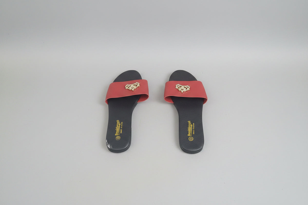 A pair of dark gray slide sandals with red straps and a gold teddy bear emblem, displayed on a dark wood floor.