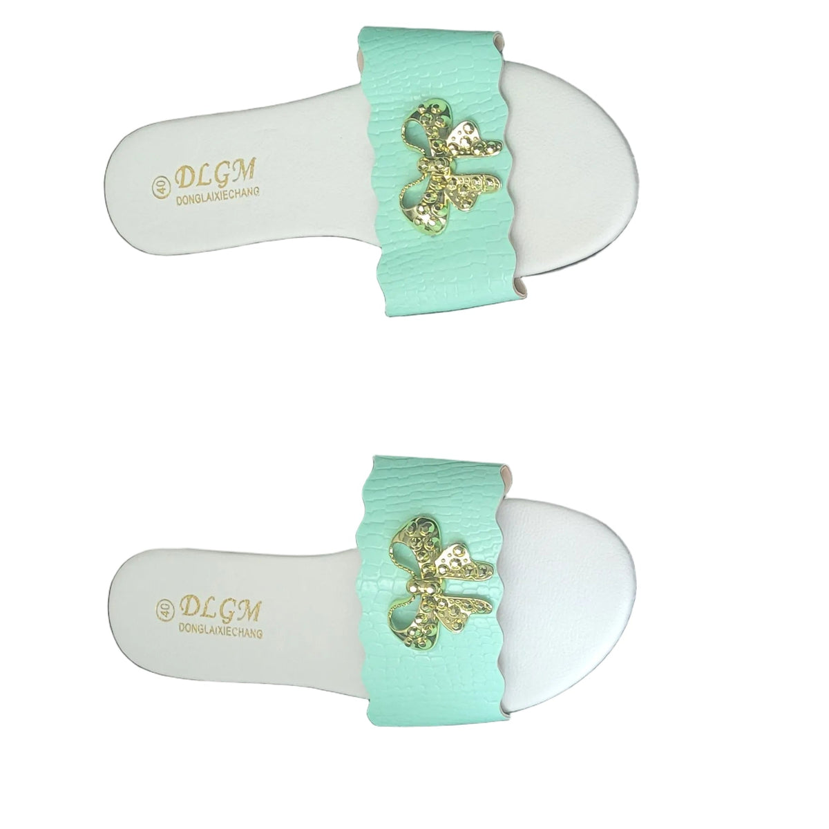 A pair of white slide sandals with mint green straps and gold-tone floral embellishments, laid flat on a dark wood floor. The brand name 'BLOOM' is visible on the footbed.
