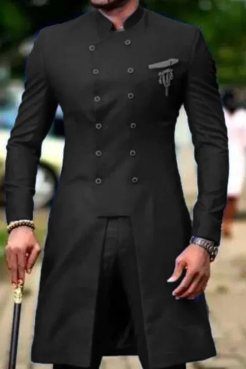 A man wearing a long black sherwani-style jacket with double-breasted buttons, a mandarin collar, and a small chest emblem, photographed outdoors with a blurred background.