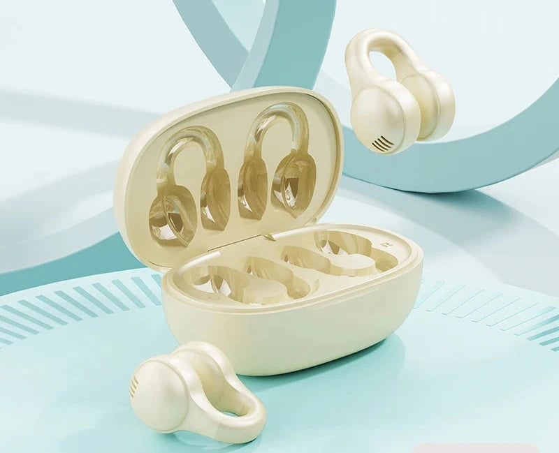 A pair of beige over-ear wireless earbuds with their matching charging case open, shown on a light blue and white studio background. One earbud is floating above the case, and another is placed in front.