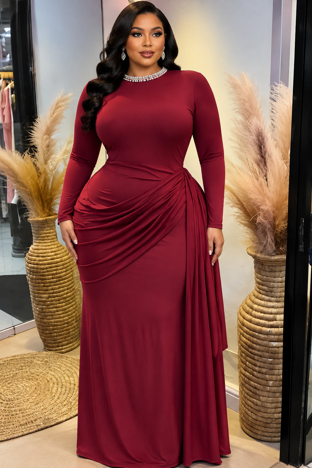 A long-sleeve red dress displayed on a mannequin torso inside a boutique. The dress has a fitted bodice, draped detailing at the waist, and a high neckline.