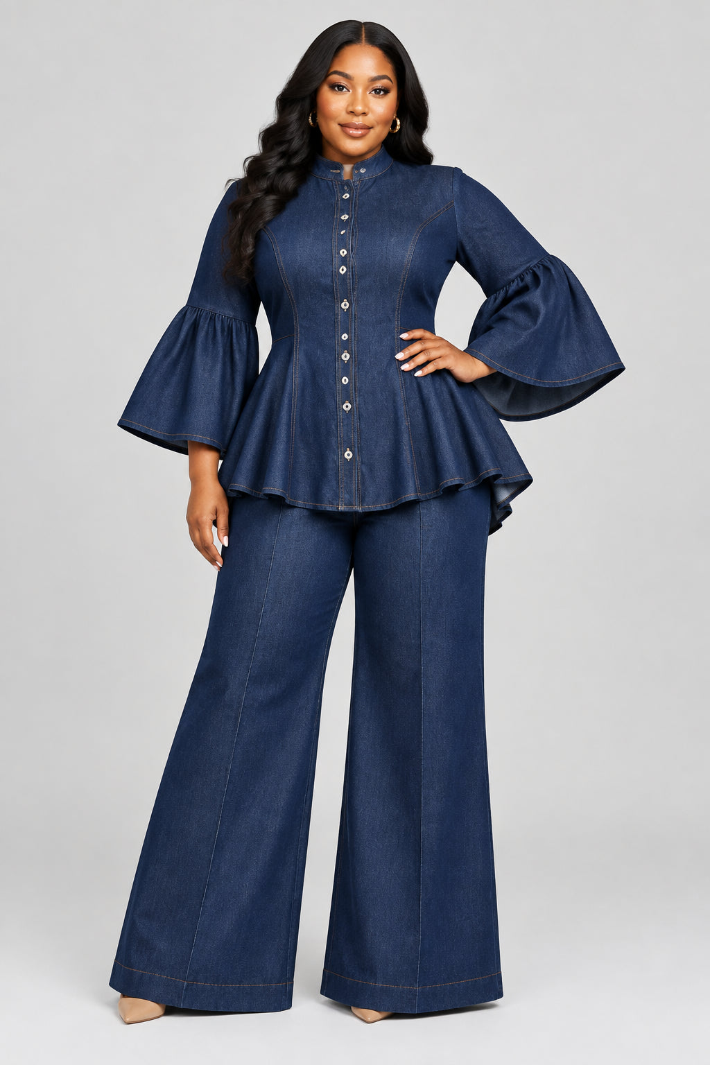 A woman modeling a matching navy blue two-piece outfit consisting of a button-front peplum blouse with ruffled elbow-length sleeves and matching wide-leg trousers. She is holding a small bright pink crocodile-embossed handbag.