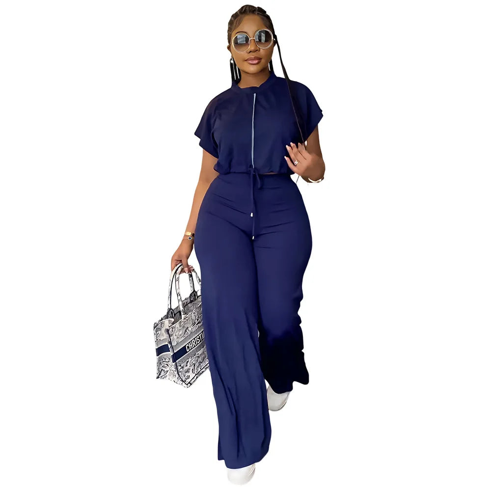 Woman in a navy blue jumpsuit holding a patterned handbag on a white background