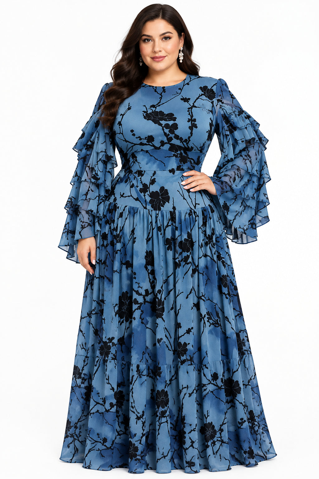 A blue long-sleeve maxi dress with a black floral branch pattern, displayed on a mannequin. The dress features a fitted bodice, a pleated ruffled waist, and voluminous sheer sleeves.