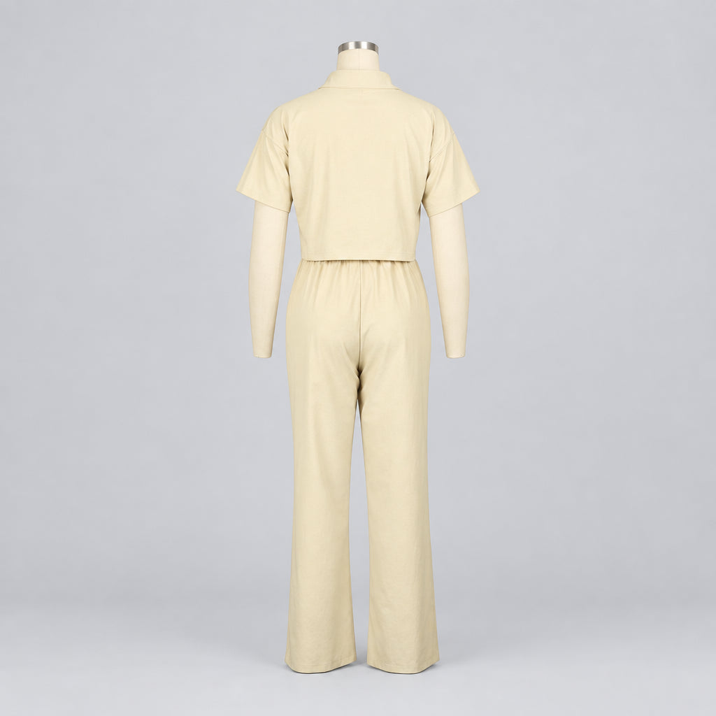 A cream-colored short-sleeve jumpsuit with wide legs, shown from the back on a mannequin against a white background. The brand name 'CM.
