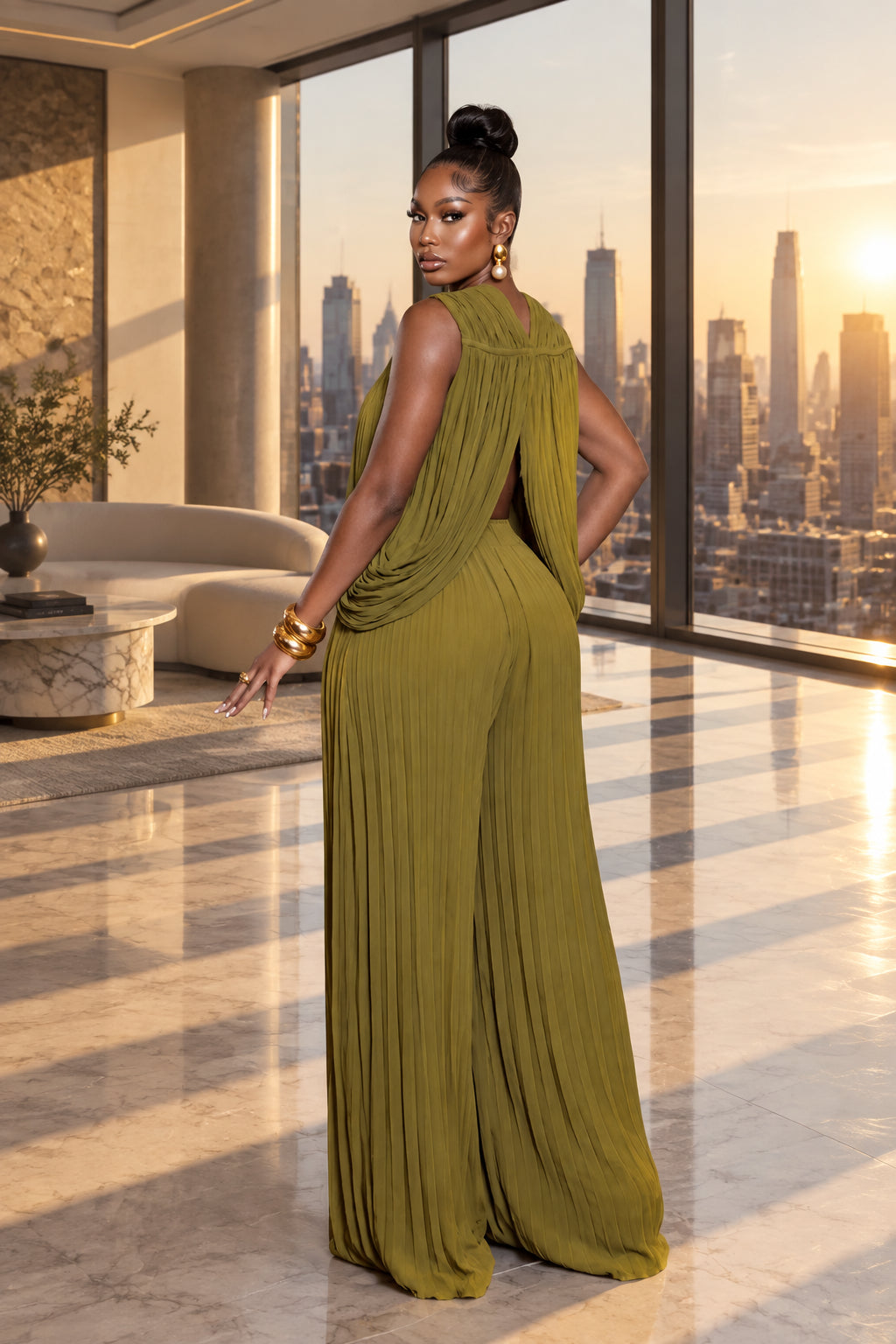 A woman wearing a sleeveless olive green pleated maxi dress with a draped back and side cutout, posing in a modern lounge bar setting with a pool table nearby.